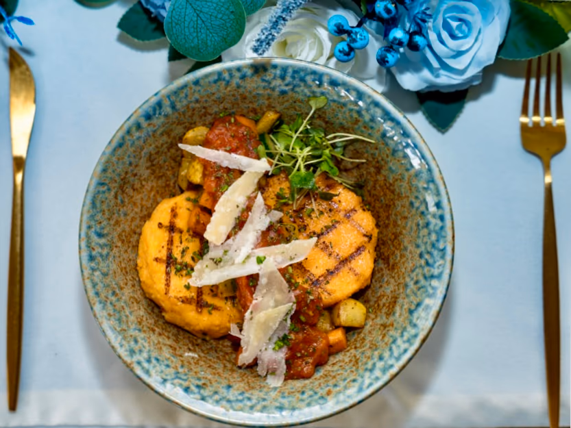 Grilled polenta cake with vegetable ragout in a blue bowl