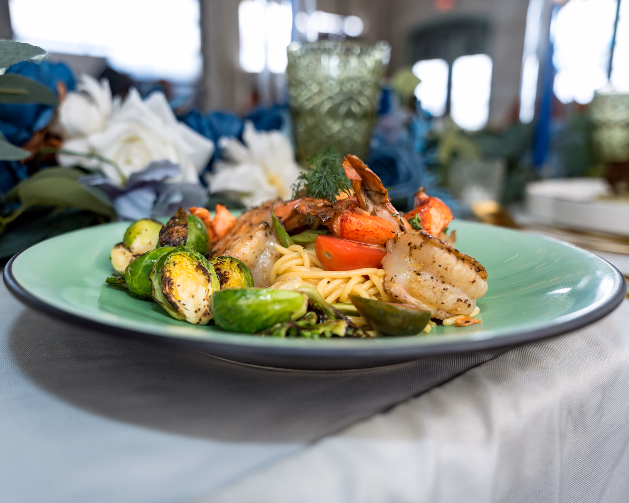 Shrimp, scallops and lobster in beurre blanc on a green plate with blue florals behind