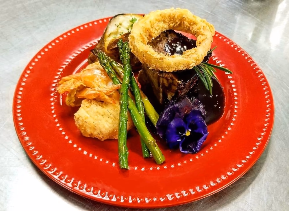 Plated steak with onion ring and asparagus on a red charger